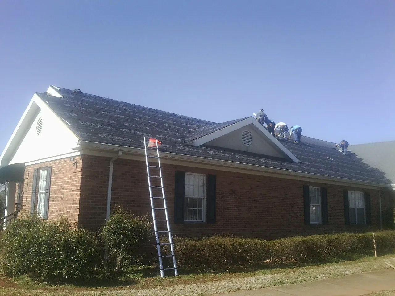 Crew tearing shingles off a brick ranch roof with a ladder set — Metal Roof Repair work by our crew in Thomasville