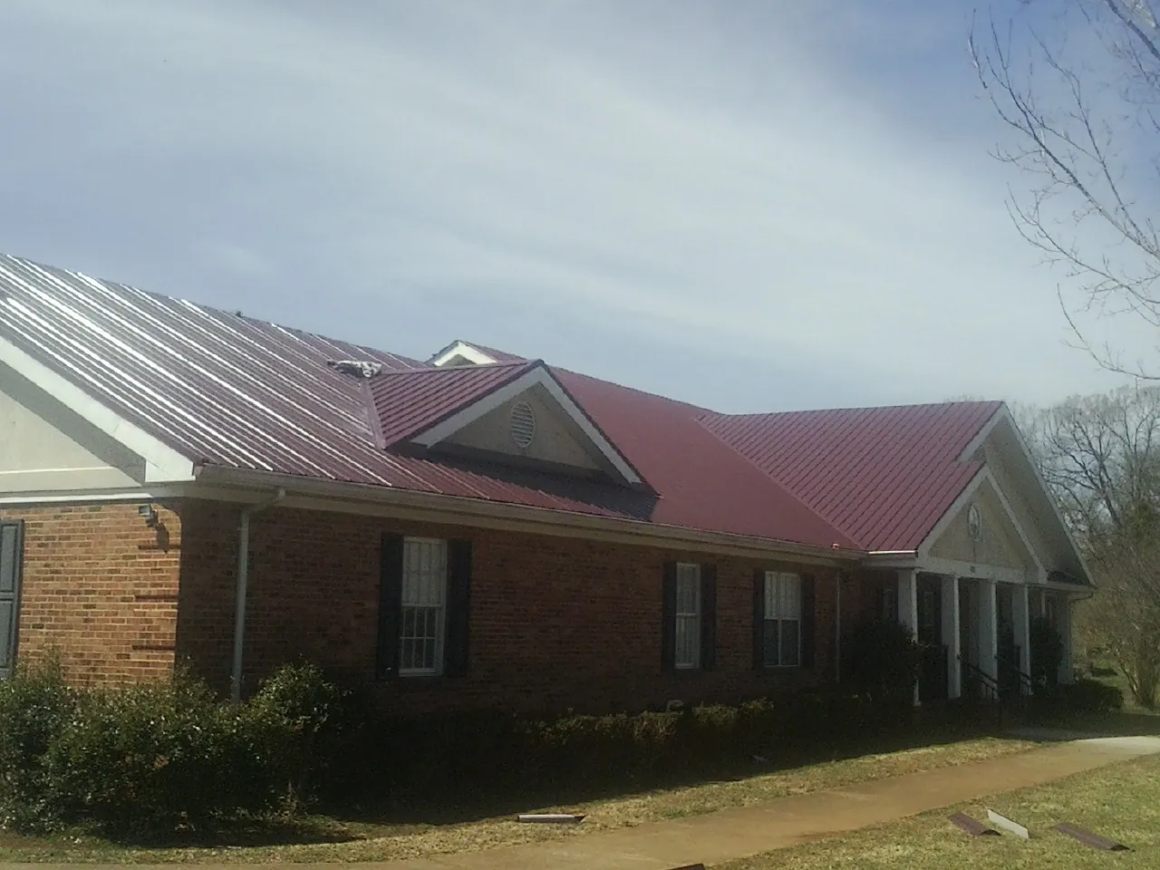 Red metal roof with gabled entries on a long brick building, from a Hail Damage Roof Repair job in Thomasville