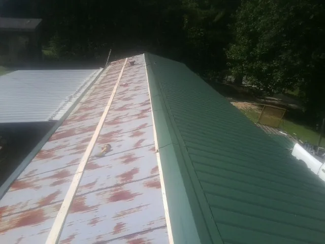 Old rusted panels beside newly installed green metal roofing — Wind Damage Roof Repair by Roofing Brothers in Thomasville